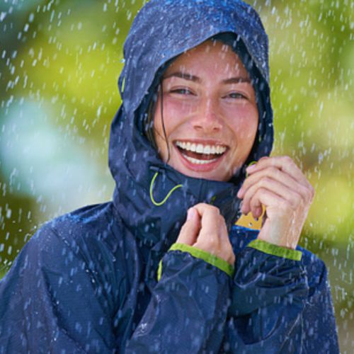 Lachende Frau in Regenjacke im Regen